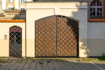 Closed metal gate and side door in a wall, with pigeons on a cobbled courtyard. Classic urban...