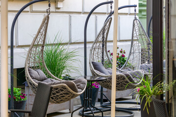 Modern hanging egg chairs with soft cushions on a stylish outdoor terrace, surrounded by potted...