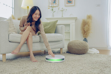 Young asian woman doing housework using automatic vacuum cleaner clean carpet and wooden floor...
