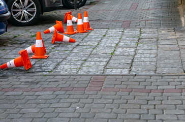 Scattered orange traffic cones placed to block access to a gate on a city sidewalk paved with...