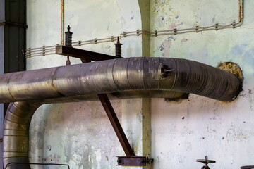Section of an old industrial installation with a large insulated pipe running along a damaged wall...