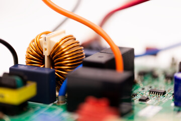 Close-up of a copper coil inductor mounted on a green PCB, surrounded by relays, connectors, and...