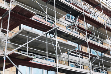 Building under renovation process. Metal scaffolding on construction site. Exterior wall insulation and repair. Urban maintenance in progress. Industrial framework structure in city renovation work.