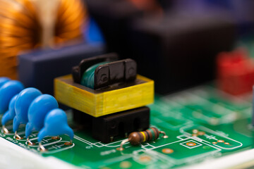 Macro image showing a yellow transformer, blue ceramic capacitors, and a resistor mounted on a...