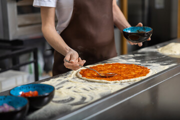 Female cooker putting filling into pizza in the kitchen