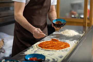 Female cooker putting filling into pizza in the kitchen