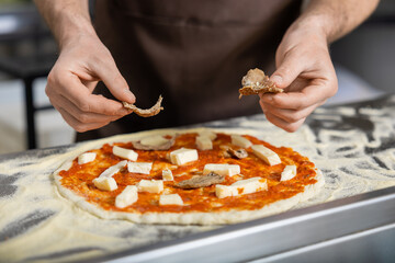 Close up picture of cookers hands putting topping o the pizza