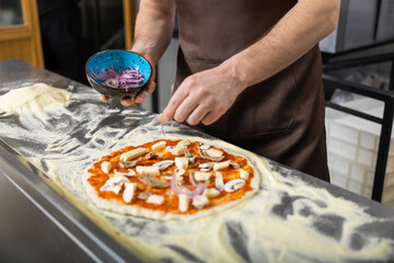 Close up picture of cookers hands putting topping o the pizza