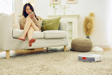 Young asian woman doing housework using automatic vacuum cleaner clean carpet and wooden floor...