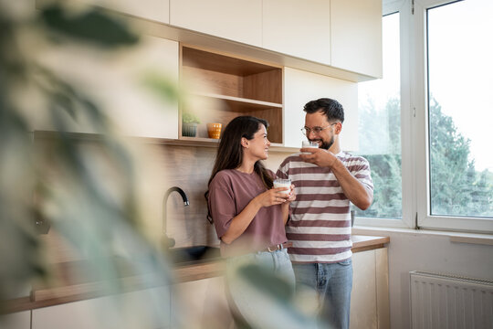Happy couple drinking milk in modern kitchen, enjoying morning routine together - Powered by Adobe