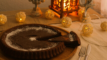 Whole chocolate tart with a slice missing surrounded by warm decorative lights