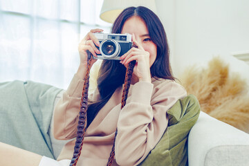 Beautiful female amateur photographer sits comfortably on a sofa holding her vintage camera and...