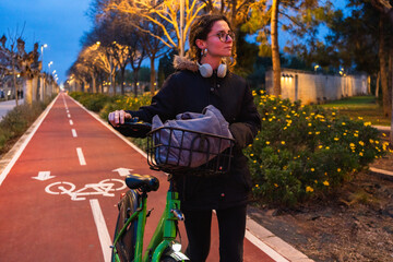 Student walking with her bicycle on a bike path at dusk, enjoying the fresh air and the urban landscape