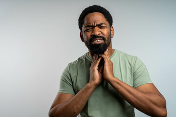 Worried young black man touching neck with discomfort, thyroid gland pain or disorder, isolated...