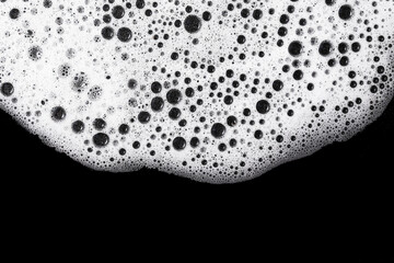 Soap foam texture closeup. White frothy bubbles on black background. Cleaning concept and hygiene...