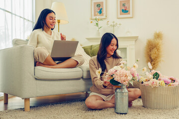 Free time lifestyle activities Arranging artificial flowers at home arranging beautiful pastel colored artificial flowers and female friend sitting sofa playing with laptop enjoying herself good mood.