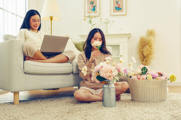 Free time lifestyle activities Arranging artificial flowers at home arranging beautiful pastel colored artificial flowers and female friend sitting sofa playing with laptop enjoying herself good mood.