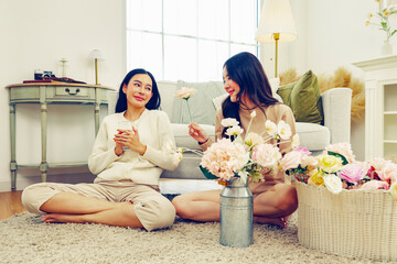 Free day lifestyle activity arranging artificial flowers at home between two asian women arranging beautiful pastel colored artificial flowers and female friend drinking coffee support good mood.