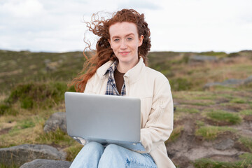 Working remotely on a laptop with a scenic landscape backdrop during a windy day in the countryside