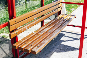 Damaged wooden bench in bus stop shelter. Broken and cracked seat slats. Public transport infrastructure in poor condition. Urban decay and vandalism sign. Neglected street furniture outdoors.