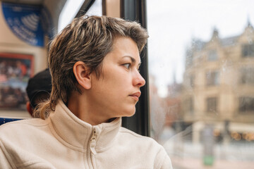Woman gazes thoughtfully out of a train window while traveling in the city during a cloudy afternoon
