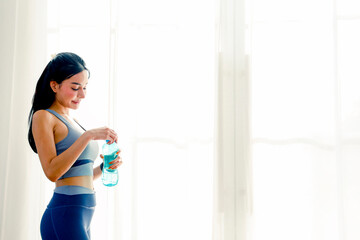 Beautiful and healthy asian woman who plays sports exercises regularly and eats healthy food is lively stands relaxes drinks clean water to hydrate and refresh herself has her own lifestyle.