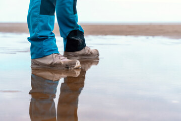 Person standing on wet sandy beach with reflections in shallow water during overcast weather near...