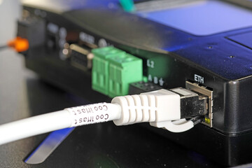 An Ethernet cable with an Rj45 connector connected to a digital equipment socket in a telecommunications rack of network equipment. 