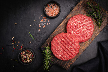 Raw steak burgers patties with ground beef and spices on a cutting board. Dark background, top view.