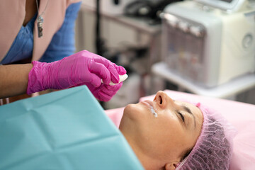 Beautician applying anesthetic cream on patient lips before permanent makeup