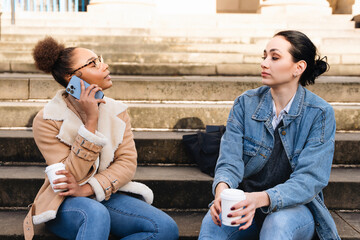 Friends enjoy conversation on steps of a historic building while sipping coffee in a city during a...
