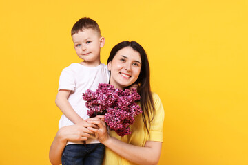 Mother and her son with bouquet of lilac flowers on yellow background, space for text
