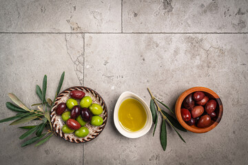 Green and black olives in a bowls and olive oil on gray background top view. Olive oil and variety...