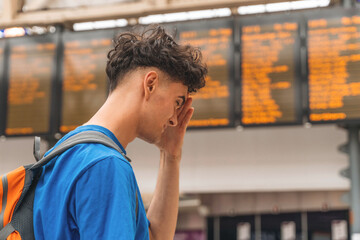 Young traveler checking train schedules at busy transit station during the day while looking concerned about delays and connections