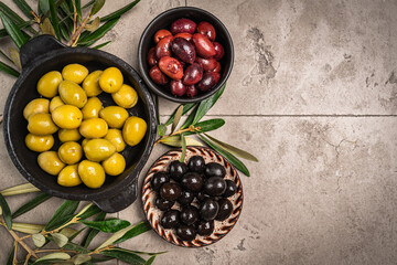 Green and black olives in a bowls and olive oil on gray background top view. Olive oil and variety...