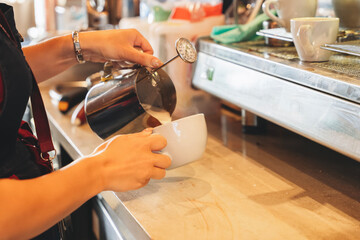 Barista pouring steamed milk into a cup while preparing coffee at a cozy cafe during a sunny...