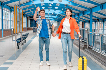 Obraz premium Couple walking hand in hand through modern train station with luggage, enjoying travel adventure on bright sunny day