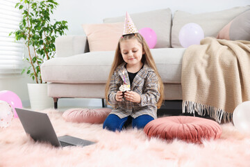 Birthday celebration. Little girl with cupcake having video call via laptop at home