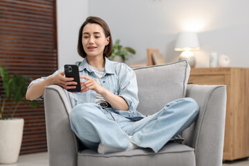 Obraz premium Woman using modern smartphone in armchair at home