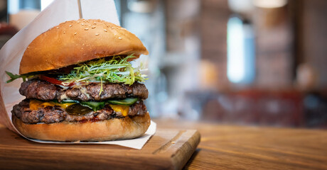 Delicious burger on the background of the interior of the burger shop. Fresh hamburger with salad, meat, cheese and sauce on the table.
