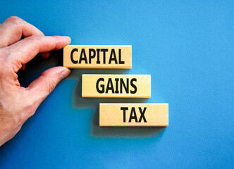 Capital gains tax symbol. Concept words Capital gains tax on beautiful wooden block. Businessman's hand. Beautiful blue background. Business and capital gains tax concept. Copy space.