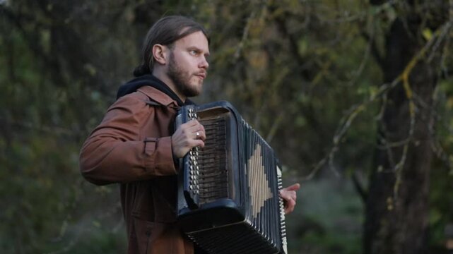 A long-haired man plays the accordion outdoors