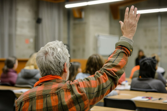 Elderly man actively participating in a classroom setting, raising his hand to ask a question among younger students.
