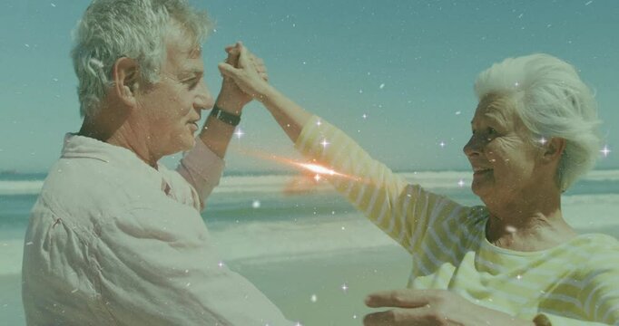 Senior man reaching and drawing woman into dancing by ebbing surf showing lifestyle sparkle overlay