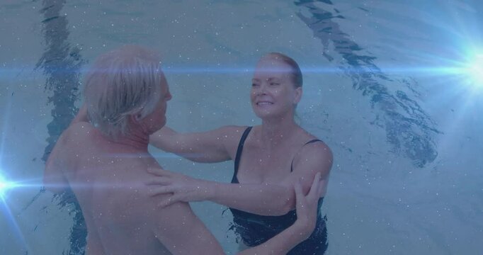 Senior couple performing fitness in pool with lane marker, man lifting arm starting underarm turn