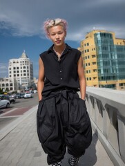 Fashionable young woman with pastel pink hair in urban setting under stormy sky, modern cityscape background