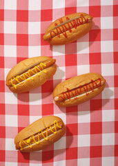 Top view of four delicious hot dogs with mustard and ketchup on a red checkered tablecloth. Classic fast food concept.