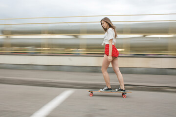Young woman riding a longboard in motion on an urban street. Dynamic summer vibe with blurred background