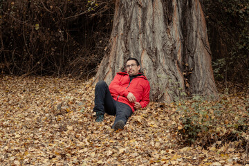 retrato de hombre recostado sobre las hojas caídas en medio del bosque en temporada de otoño