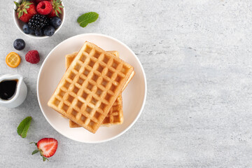 Plain waffles with fresh berries and maple syrup on a gray background. Copy space. Top view.